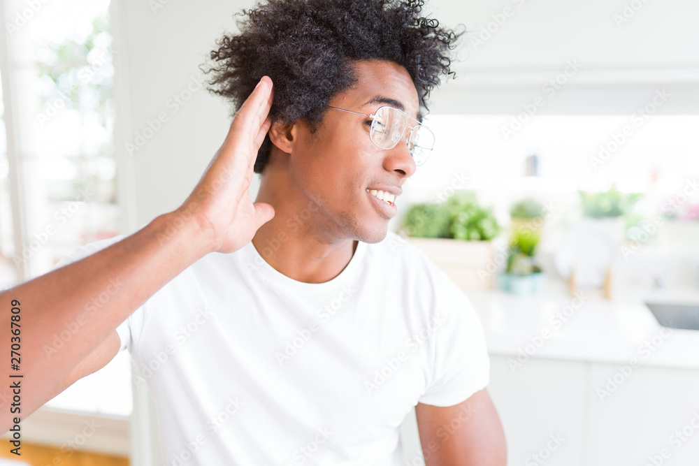 African American man wearing glasses smiling with hand over ear listening an hearing to rumor or gossip. Deafness concept. African American man wearing glasses smiling with hand over ear listening an hearing to rumor or gossip. Deafness concept.