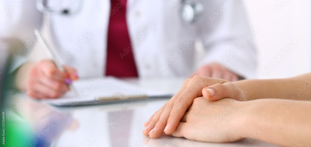 Unknown doctor woman consulting patient while filling up an application form at the desk in hospital. Just hands close-up. Medicine and health care concept