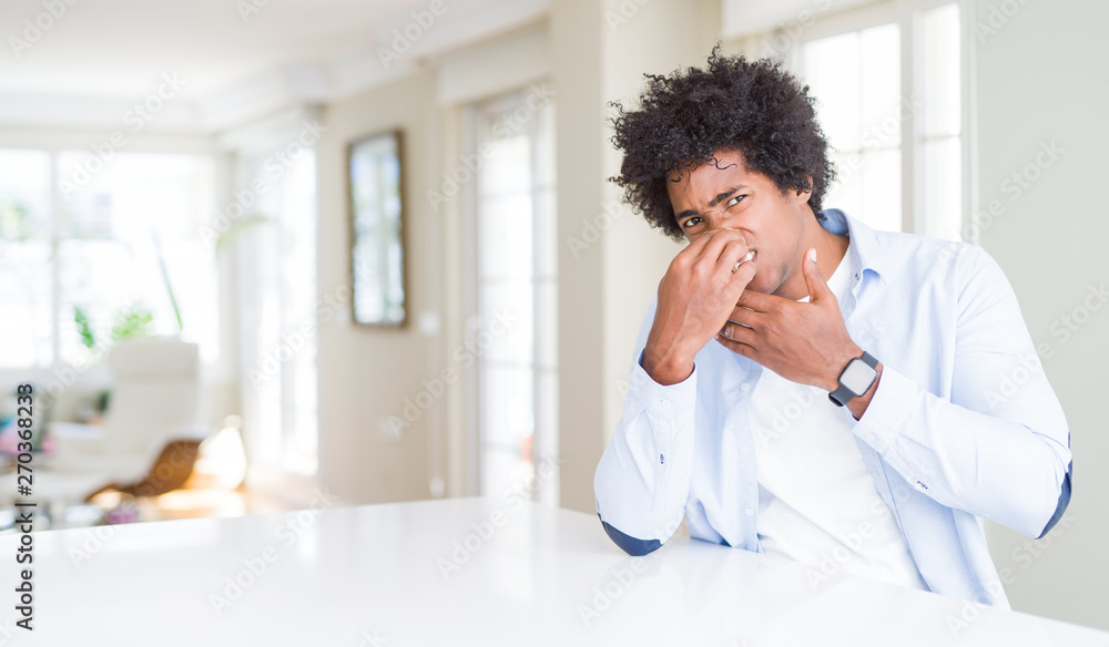 African American man at home smelling something stinky and disgusting, intolerable smell, holding breath with fingers on nose. Bad smells concept. African American man at home smelling something stinky and disgusting, intolerable smell, holding breath with fingers on nose. Bad smells concept.