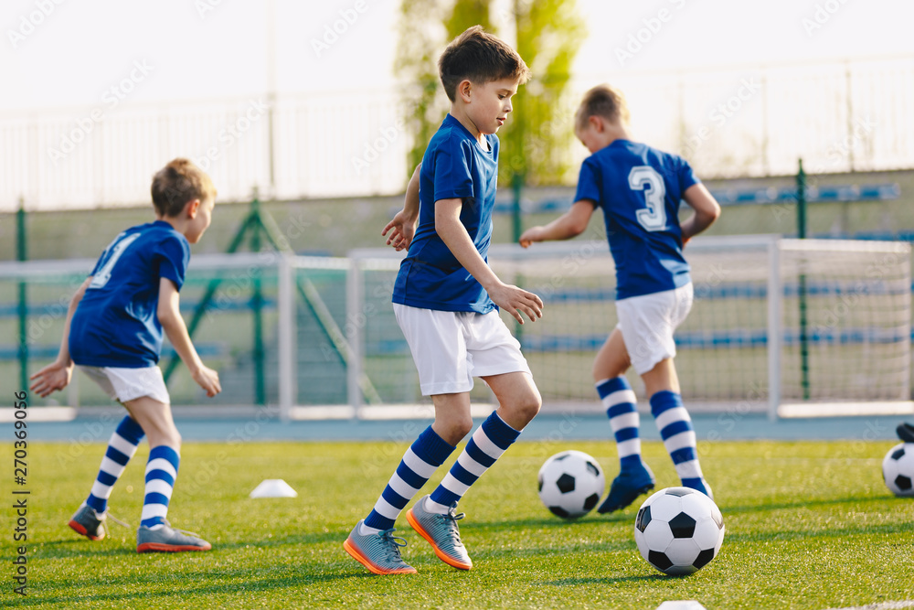 Portrait of boy in junior youth football team leading ball between cones during practice in grass field