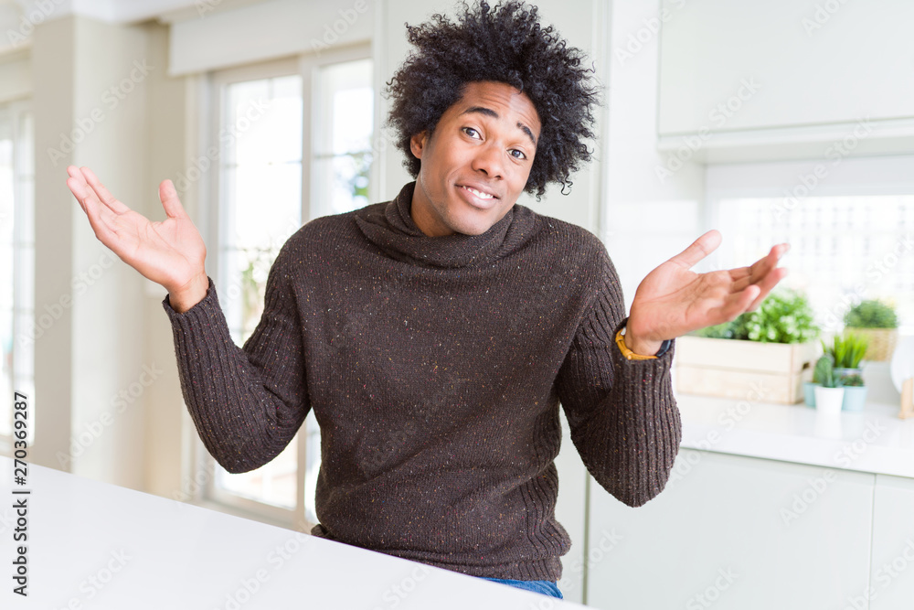 African American man wearing winter sweater clueless and confused expression with arms and hands raised. Doubt concept. African American man wearing winter sweater clueless and confused expression with arms and hands raised. Doubt concept.