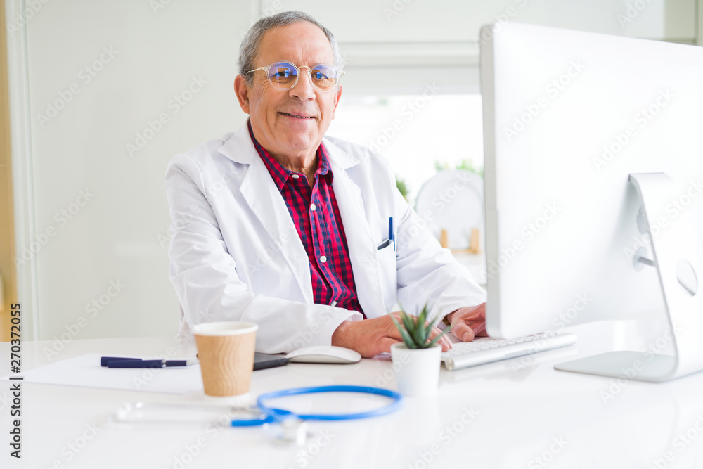 Senior doctor man at the clinic working with computer and smiling Senior doctor man at the clinic working with computer and smiling