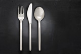 Stainless steel fork, knife and spoon cutlery or silverware set, isolated on black stone background with copy space.
