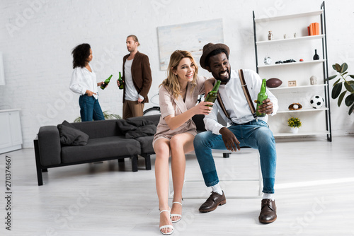 selective focus of cheerful woman smiling near african american man with beer