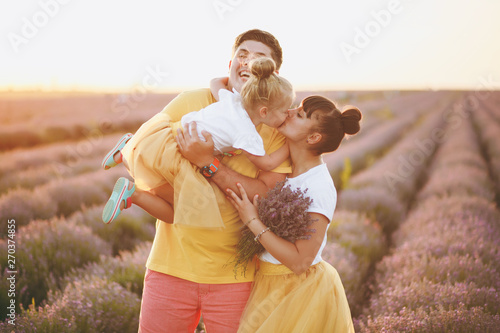 Young family in yellow clothes walk on purple lavender flower meadow field background, have fun, play with little cute child baby girl. Mother father, small kid daughter. Outdoors summer day concept.