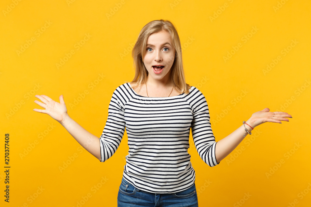 Portrait of excited young woman in striped clothes keeping mouth open, spreading hands isolated on yellow orange background in studio. People sincere emotions, lifestyle concept. Mock up copy space. Portrait of excited young woman in striped clothes keeping mouth open, spreading hands isolated on yellow orange background in studio. People sincere emotions, lifestyle concept. Mock up copy space.