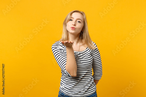 Portrait of pretty young woman in striped clothes looking camera, blowing sending air kiss isolated on yellow orange wall background. People sincere emotions, lifestyle concept. Mock up copy space.