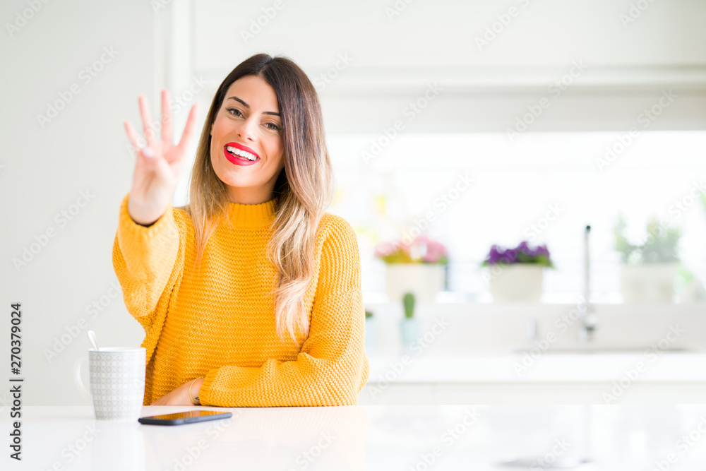 Young beautiful woman drinking a cup of coffee at home showing and pointing up with fingers number four while smiling confident and happy. Young beautiful woman drinking a cup of coffee at home showing and pointing up with fingers number four while smiling confident and happy.