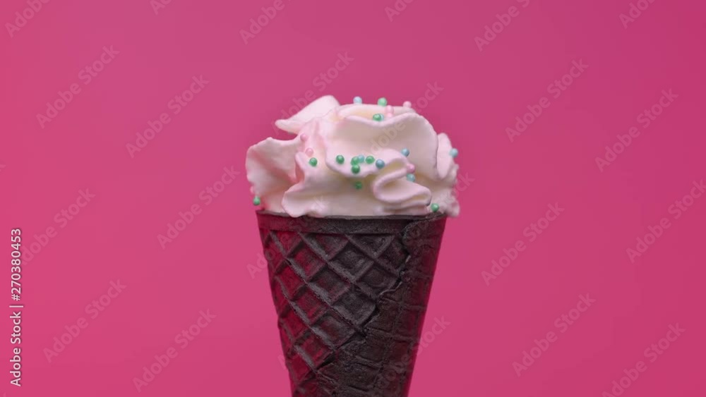 Soft ice cream in black cone decorated with colorful sprinkles over pink background Soft ice cream in black cone decorated with colorful sprinkles over pink background