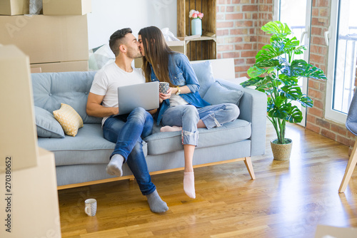 Young couple moving to a new home relaxing sitting on the sofa using computer laptop, smiling happy for moving to new apartment