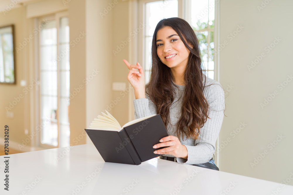 Young woman reading a book very happy pointing with hand and finger to the side Young woman reading a book very happy pointing with hand and finger to the side