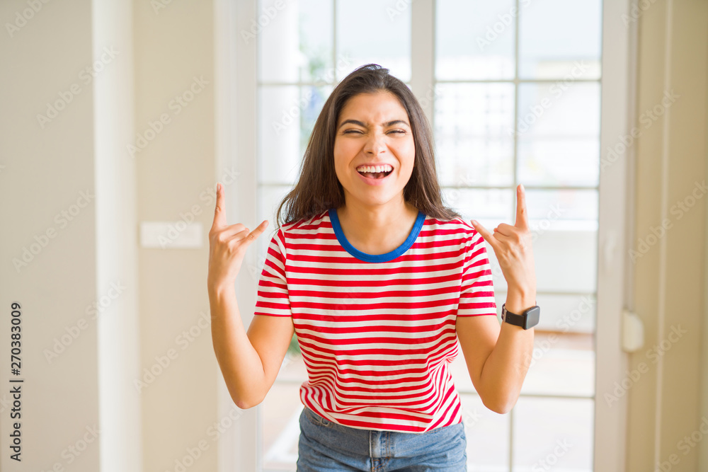 Young beautiful woman wearing casual t-shirt shouting with crazy expression doing rock symbol with hands up. Music star. Heavy concept. Young beautiful woman wearing casual t-shirt shouting with crazy expression doing rock symbol with hands up. Music star. Heavy concept.