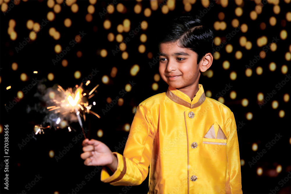 Cute Indian child celebrating Diwali festival with cracker and sparkle Cute Indian child celebrating Diwali festival with cracker and sparkle