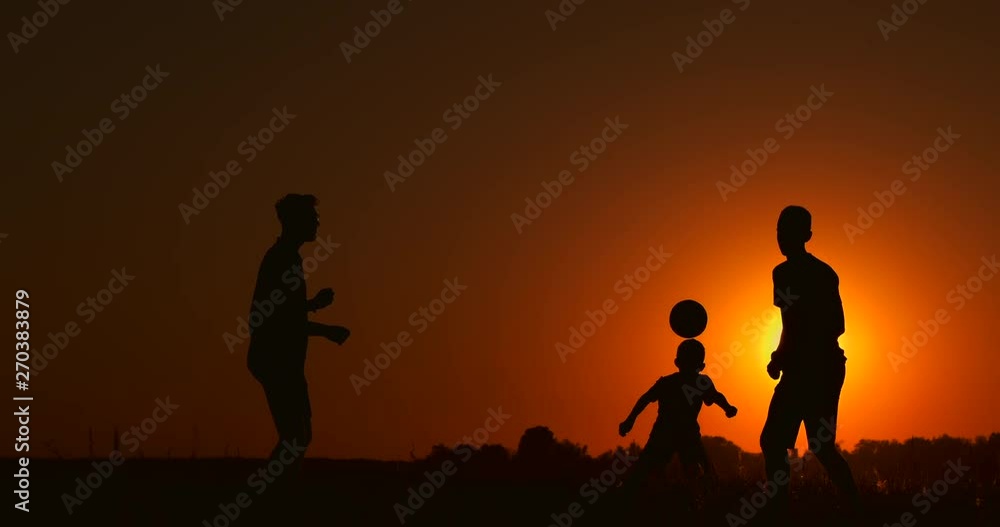 Three boys playing soccer at sunset. Silhouette of children playing with a ball at sunset. The concept of a happy family Three boys playing soccer at sunset. Silhouette of children playing with a ball at sunset. The concept of a happy family