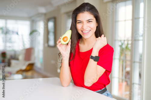 Young woman eating healthy avocado screaming proud and celebrating victory and success very excited, cheering emotion