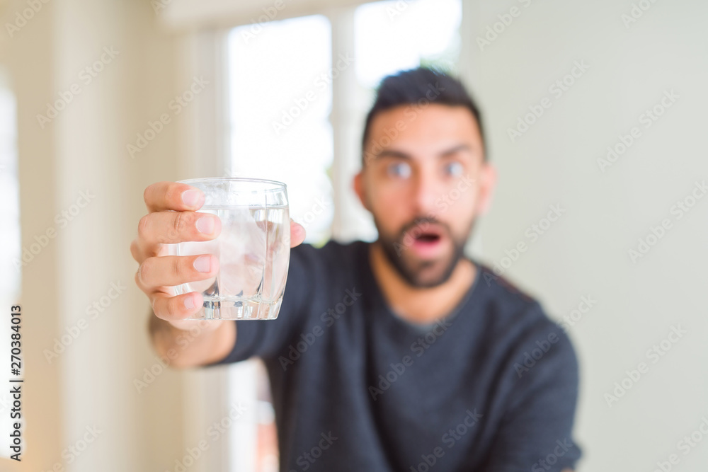 Handsome hispanic man drinking a fresh glass of water scared in shock with a surprise face, afraid and excited with fear expression Handsome hispanic man drinking a fresh glass of water scared in shock with a surprise face, afraid and excited with fear expression