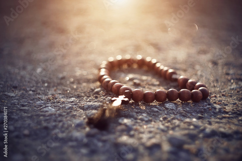 Wooden Catholic rosary with a cross lie on a rocky surface, illuminated by sunlight, as an inspiration from above