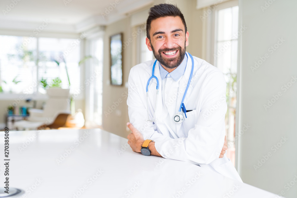 Handsome hispanic doctor man wearing stethoscope at the clinic happy face smiling with crossed arms looking at the camera. Positive person.