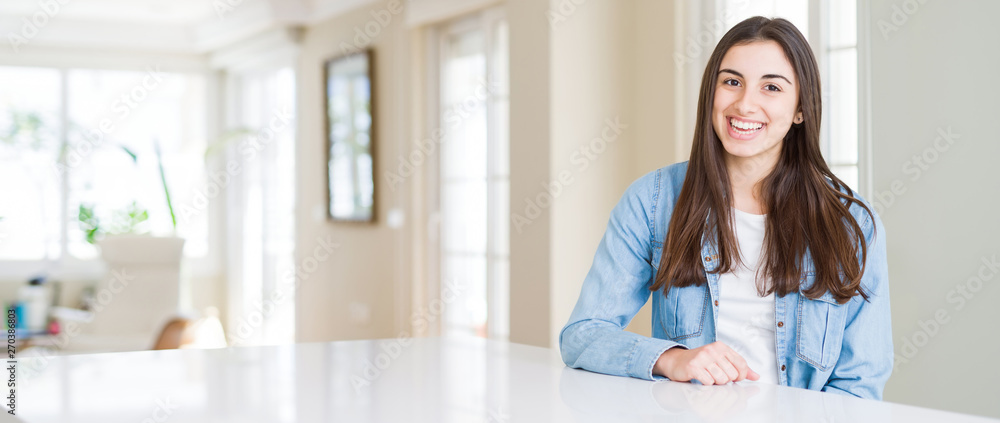 Wide angle picture of beautiful young woman sitting on white table at home with a happy and cool smile on face. Lucky person. Wide angle picture of beautiful young woman sitting on white table at home with a happy and cool smile on face. Lucky person.