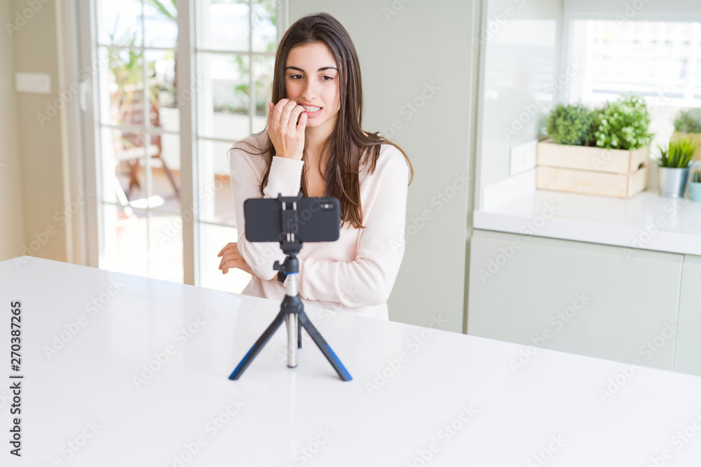 Beautiful young woman recording selfie video with smartphone webcam looking stressed and nervous with hands on mouth biting nails. Anxiety problem. Beautiful young woman recording selfie video with smartphone webcam looking stressed and nervous with hands on mouth biting nails. Anxiety problem.
