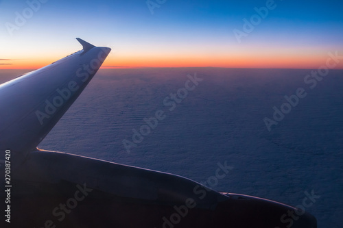 The wing of the airplane above the clouds closeup at sunset, view from the porthole