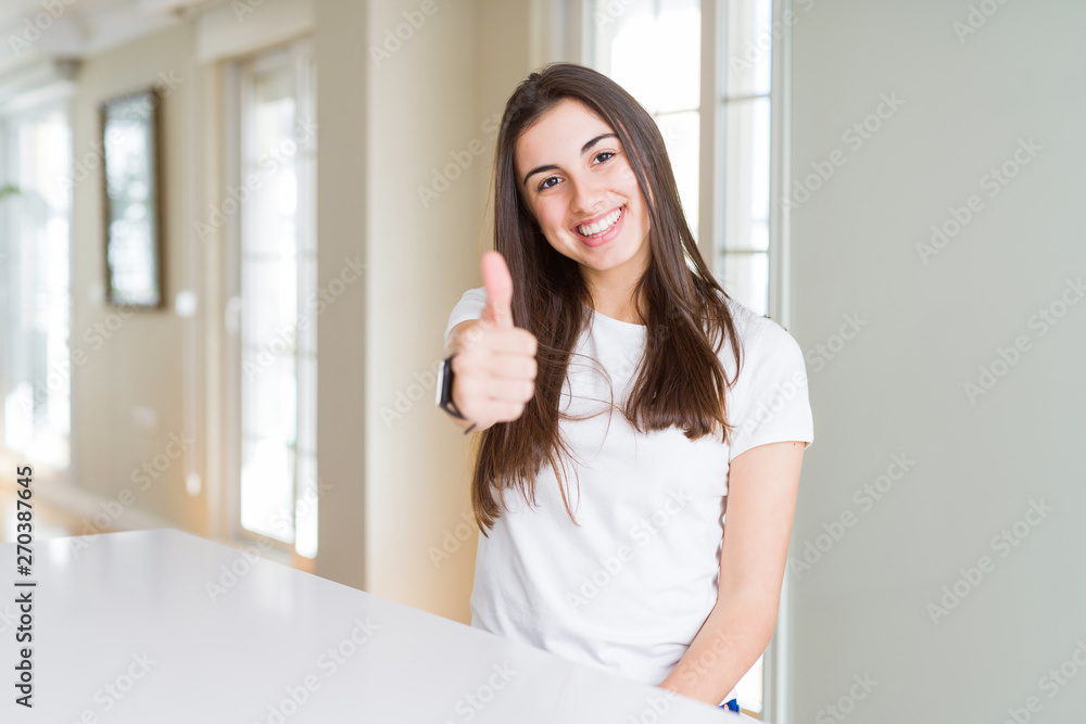 Beautiful young woman wearing casual white t-shirt doing happy thumbs up gesture with hand. Approving expression looking at the camera with showing success.