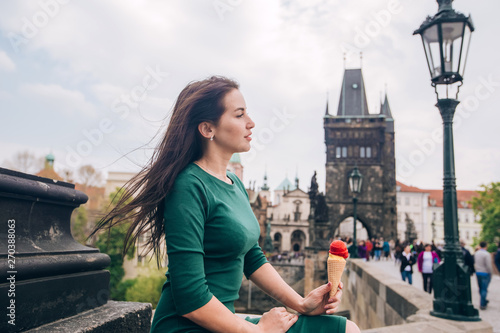 Photography Молодая брюнетка женщина, сидя расслабленной и едят мороженое на стенах Карлова моста, над рекой Влтава, город Прага, в Чешской Республике