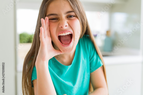 Beautiful young girl kid wearing green t-shirt shouting and screaming loud to side with hand on mouth. Communication concept.