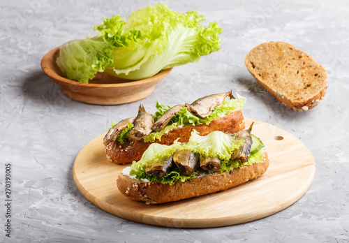 Sprats sandwiches with lettuce and cream cheese on wooden board on a gray concrete background.