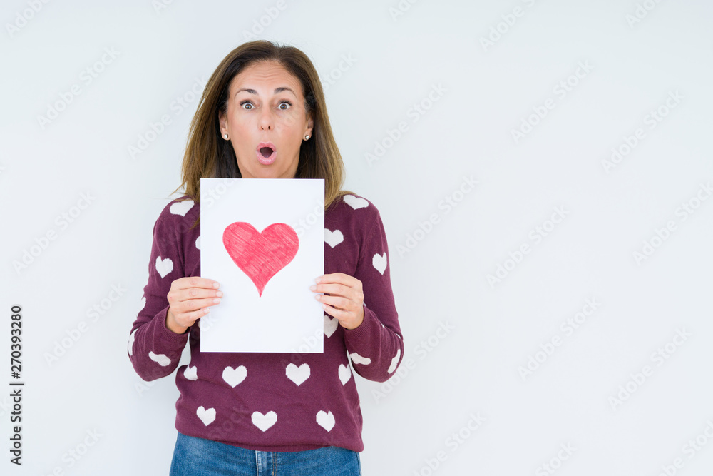 Middle age woman holding card gift with red heart over isolated background scared in shock with a surprise face, afraid and excited with fear expression Middle age woman holding card gift with red heart over isolated background scared in shock with a surprise face, afraid and excited with fear expression