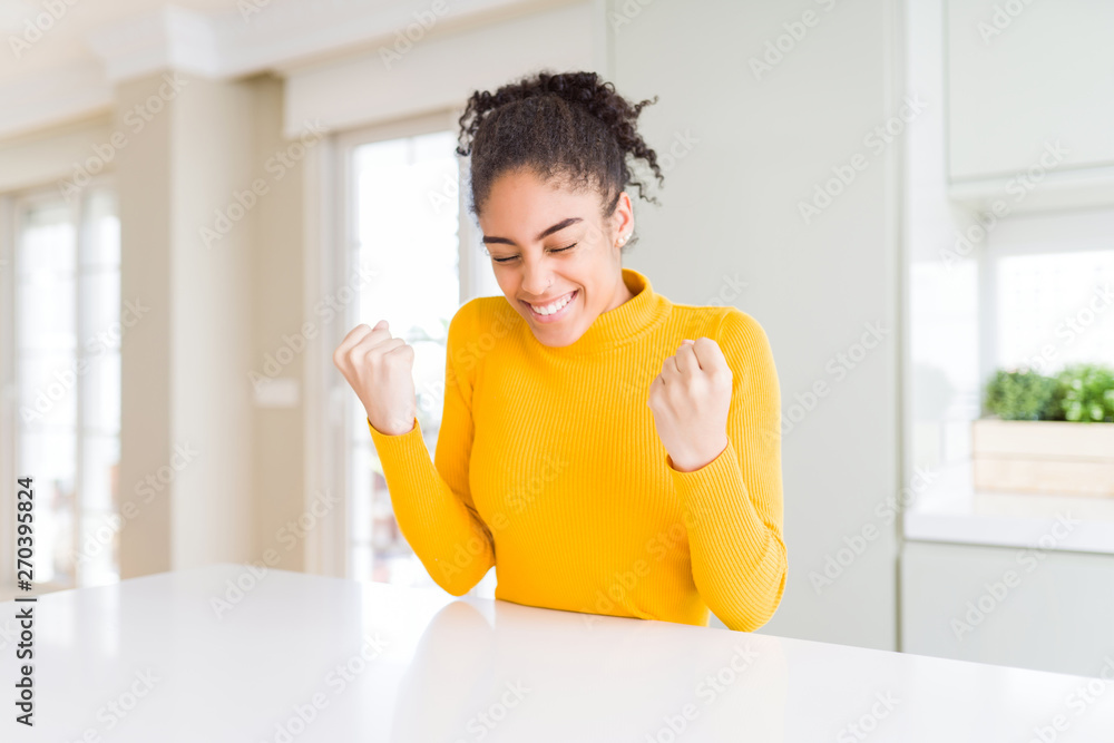 Beautiful african american woman with afro hair wearing a casual yellow sweater very happy and excited doing winner gesture with arms raised, smiling and screaming for success. Celebration concept.
