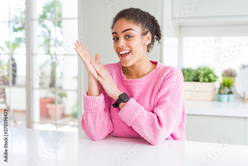 Beautiful african american woman with afro hair wearing casual pink sweater clapping and applauding happy and joyful  smiling proud hands together