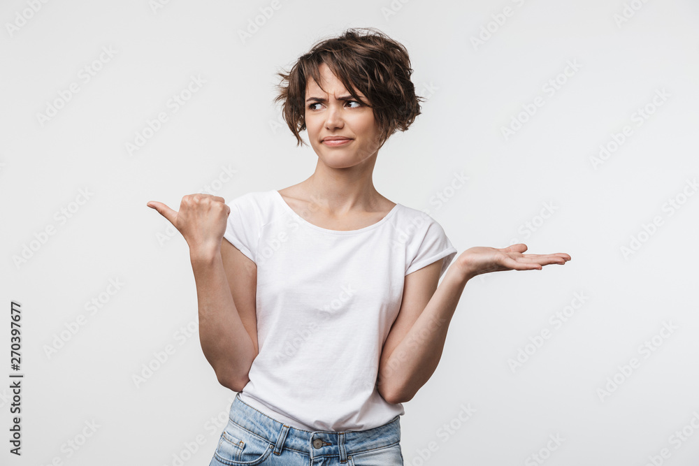Image of confused woman with short hair in basic t-shirt pointing finger aside at copyspace Image of confused woman with short hair in basic t-shirt pointing finger aside at copyspace