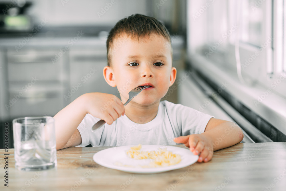 a little boy eats pasta in the form of a spiral in the afternoon in the kitchen on their own a little boy eats pasta in the form of a spiral in the afternoon in the kitchen on their own