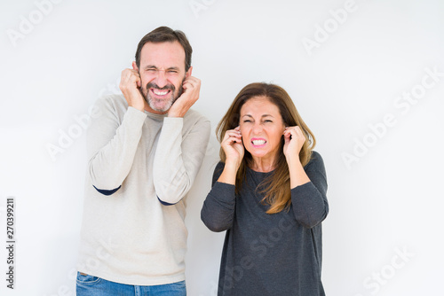 Beautiful middle age couple in love over isolated background covering ears with fingers with annoyed expression for the noise of loud music. Deaf concept.