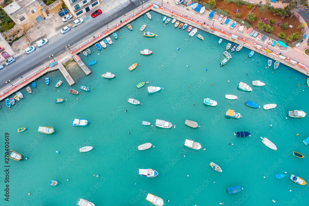 Traditional eyed colorful boats in the harbor of Mediterranean fishing village, aerial view Marsaxlokk, Malta.