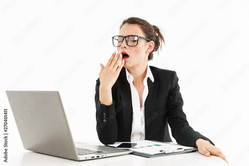 Photo of pretty female worker businesswoman dressed in formal wear yawning while working on laptop in office Photo of pretty female worker businesswoman dressed in formal wear yawning while working on laptop in office
