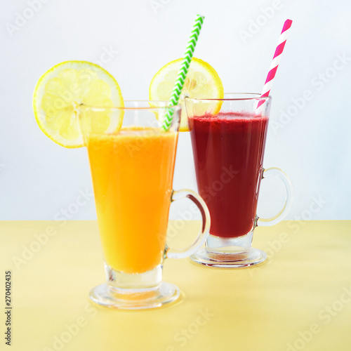 Two different colors cocktails in glass cups with straw and lemon slice. Healthy smoothies, yellow and white background.