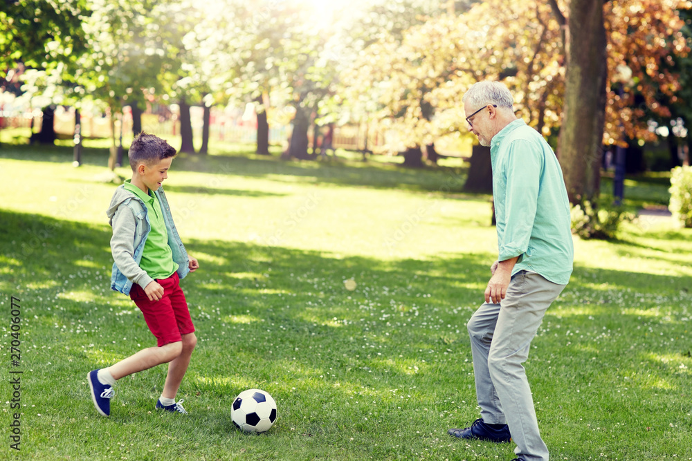 family, generation, game, sport and people concept - happy grandfather and grandson playing football at summer park family, generation, game, sport and people concept - happy grandfather and grandson playing football at summer park