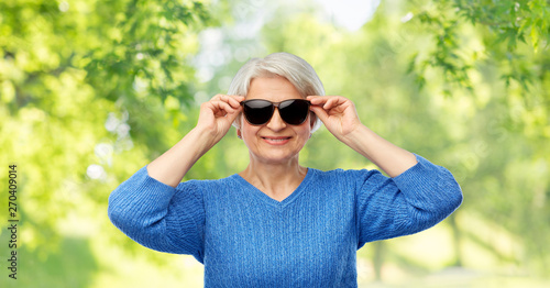 valentine's day, summer and old people concept - portrait of smiling senior woman in red black sunglasses over green natural background