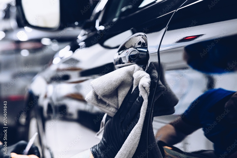 Man worker in car wash polishing car with cloth