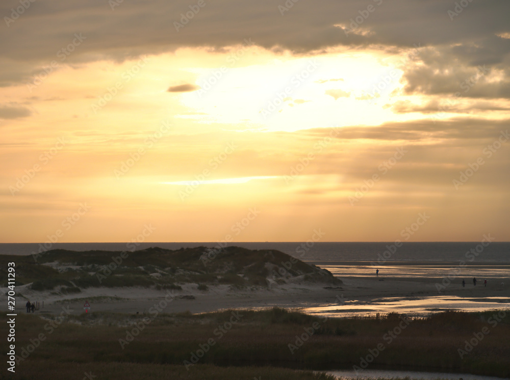 Obraz premium Sunset behind the clouds over dunes and beach in Sankt Peter-Ording