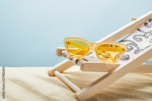 yellow sunglasses and deck chair on sand on blue background