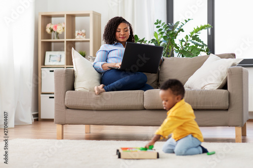 family, motherhood and people concept - happy african american mother using laptop computer and little baby son playing with toy blocks kit at home