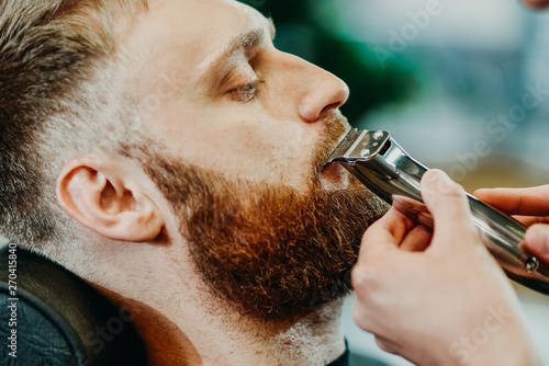 the barber cuts his beard to a man in the salon