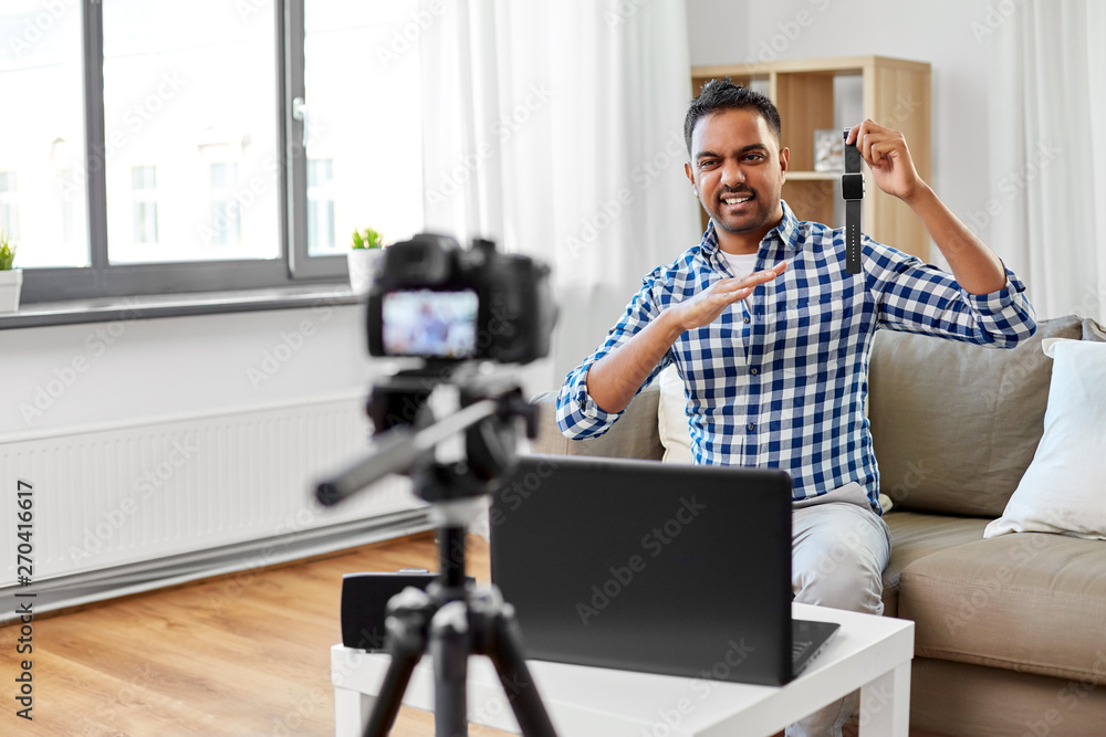 blogging, videoblog and technology concept - displeased indian male blogger with camera recording video review of smart watch at home blogging, videoblog and technology concept - displeased indian male blogger with camera recording video review of smart watch at home