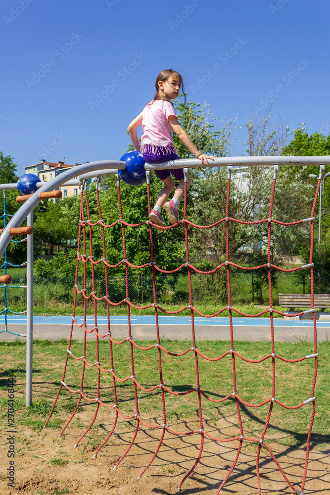 Fototapeta premium teenage girl playing with motor activity developer toys like rope wall and spider web at the playground