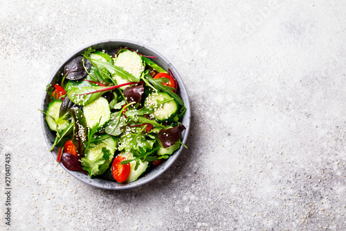 Fototapeta Naklejka Na Ścianę i Meble -  Vegetable salad in a glass bowl with greens, olive oil and sesame  on a gray background.Vegetarian. Concept for a tasty and healthy meal. Copy space for Text.Top view.