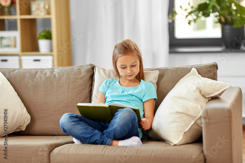 people, childhood and leisure concept - little girl reading book at home