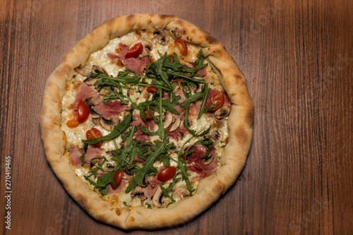 top view of whole pizza with arugula, ham, mushrooms and tomatoes